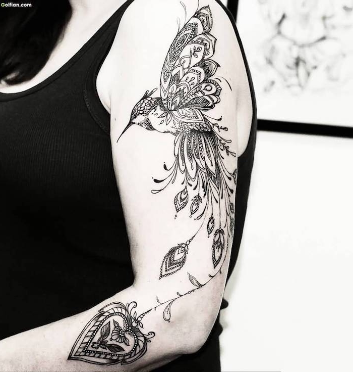 junge frau mit einer hand mit einem großen schwarzen tattoo arm mit einem fliegenden schwarzen vogel mit schwarzen langen federn und einem kerzen mit kleinen blättern