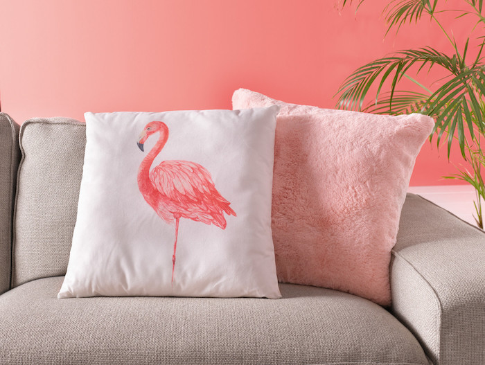 eingraues sofa mit einem pinken kissen und einem kleinen weißen kissen mit einer pinken flamingo mit pinken federn, flamingo deko