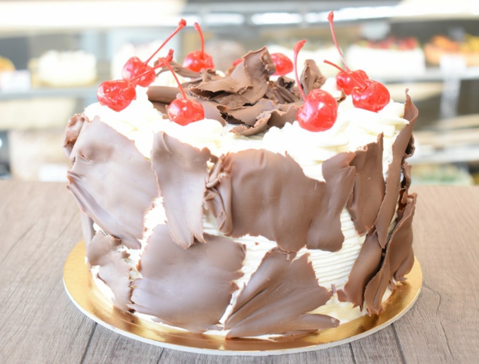 eine weiße Torte mit Schokoladen Deko und kleine Sauerkirschen, ausgefallene Torte
