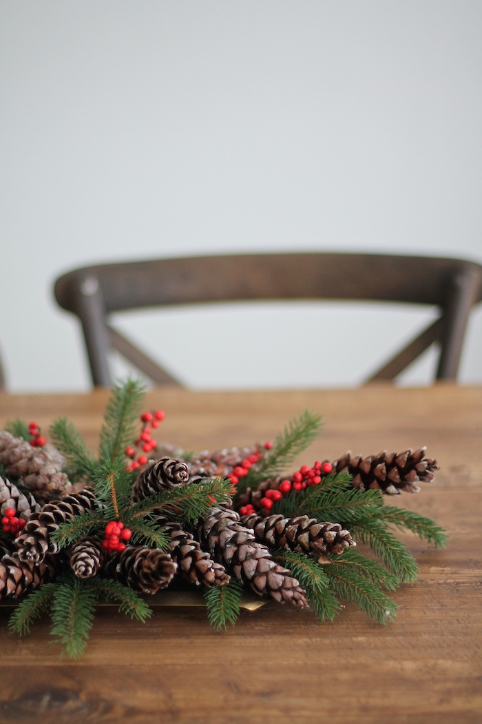 eine weiße wand und ein brauner stuhl und ein tisch aus holz mit einem adventskranz mit vidlen langen braunen tannenzapfen und mit grünen ästen und ilex, einen advenstkranz basteln, basteln mit v weihnachten 