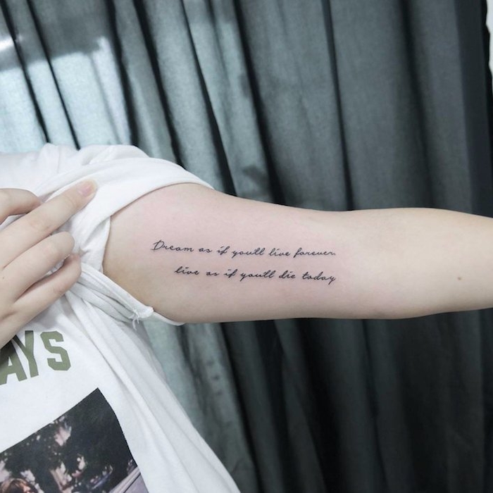 graue vorhänge und eine frau mit einem weißen t-shirt und mit einer hand mit einem schriftarten tattoo arm