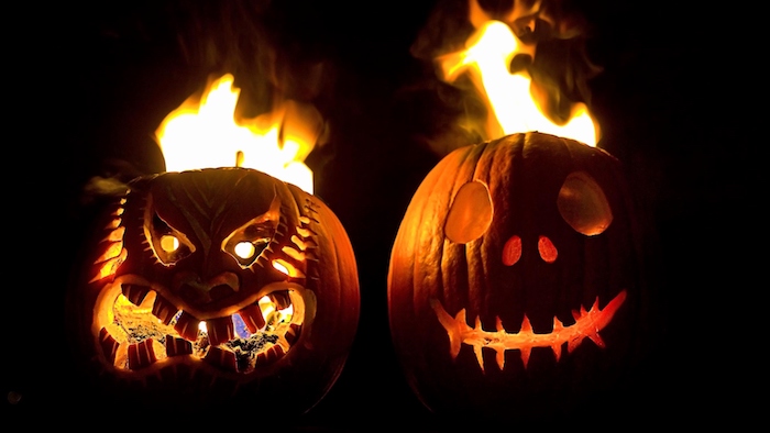 zwei brennende große orange halloween kürbisse, gruselige kürbisgesichter mit großen augen und schwarzen zähnen und mit feuer