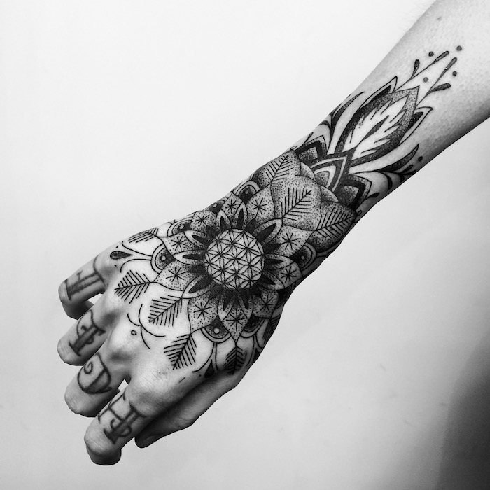 henna tattoos für frauen, eine weiße wand und eine hand mit einem großen schwarzen tattoo mit blumen und blättern