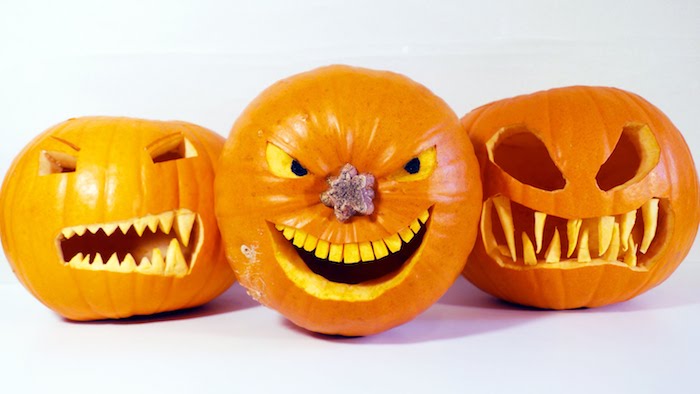 drei orange halloween kürbisse mit gruseligen kürbisgesichtern mit scharfen gelben zähnen und augen, gruselige kürbsgesichter vorlagen 