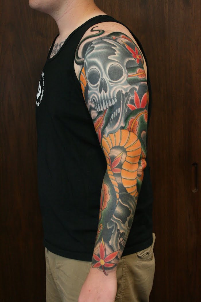 tattoo arm mit einem großen grauen totenkopf aus metall und mit schwarzen augen, tattoo mit vielen kleinen roten blumen, ein junger mann mit einem bunten arm tattoo