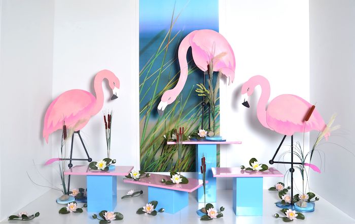 ein wandbild mit meer und grünen pflanzen, drei dekorative große pinke flamingos und weiße blumen mit grünen blättern