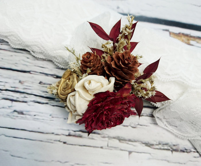 eine tischdeko mit vielen kleinen weißen rosen, roten und goldenen blumen und nzwei kleinen braunen tannenzapfen
