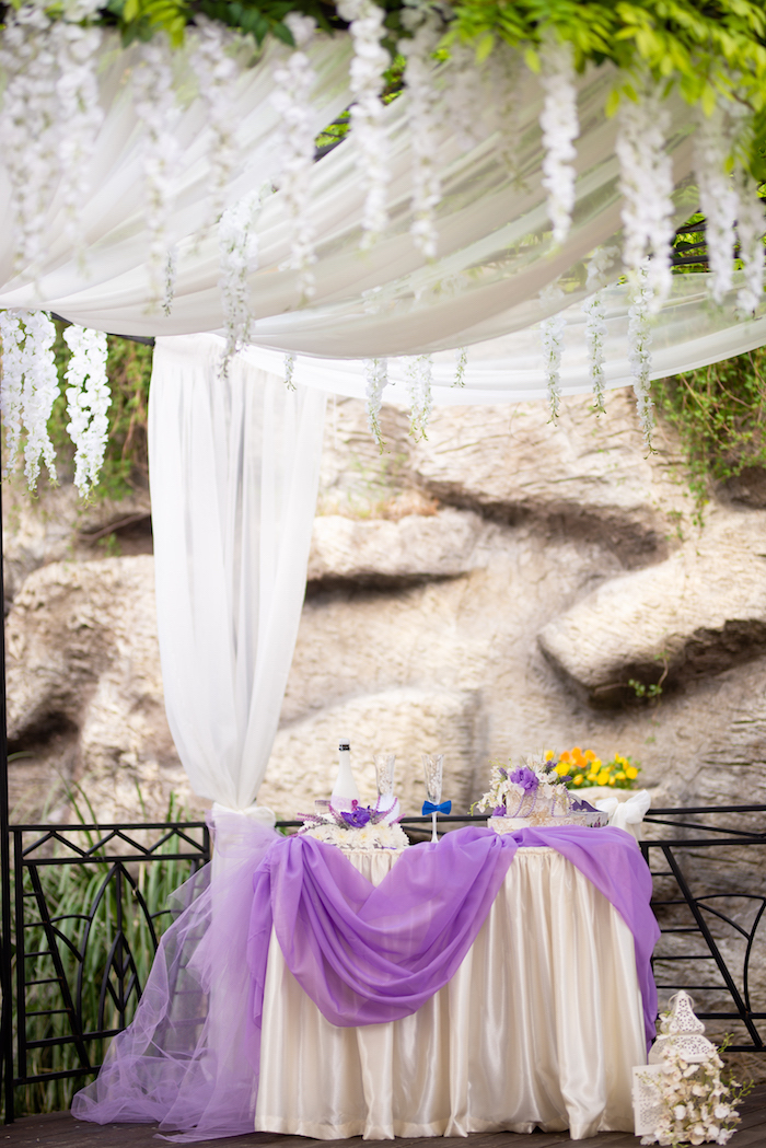 Hochzeitsfeier im Garten, weiße Tischdecke mit lila Tüll, Weinglas mit blauer Fliege