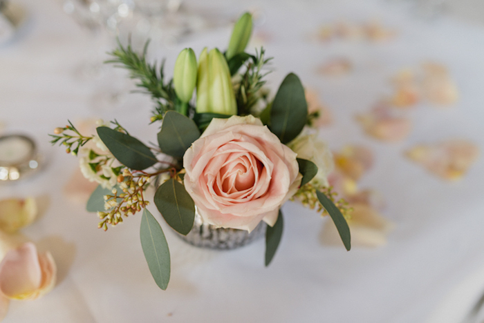 Kleiner Strauß aus Rosen und Lilien, Blütenblätter auf dem Tisch, weiße Tischdecke