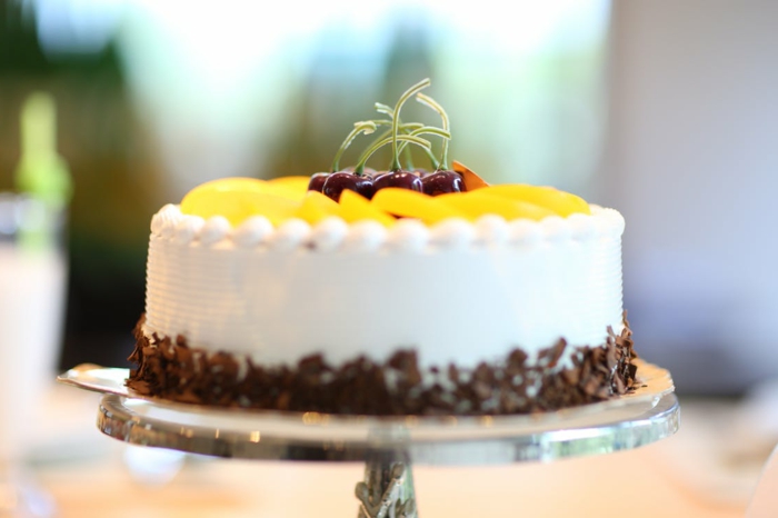 Geburtstagstorte Rezept, eine weiße Torte mit gelben Früchten und Kirschen gedeckt