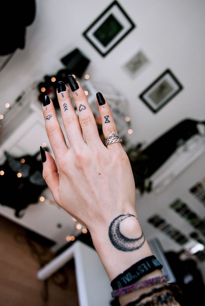 Tattoos an jedem Finger, Mond am Handgelenk, schwarzer Nagellack, silberne Ringe
