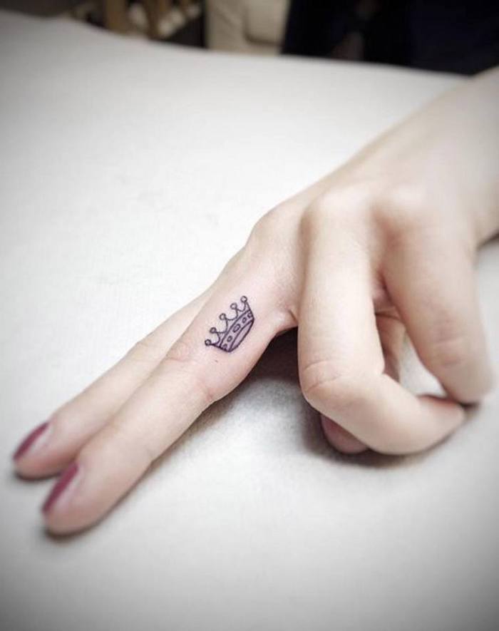 Kleines Tattoo am Mittelfinger, Krone Tattoo am Finger, roter Nagellack