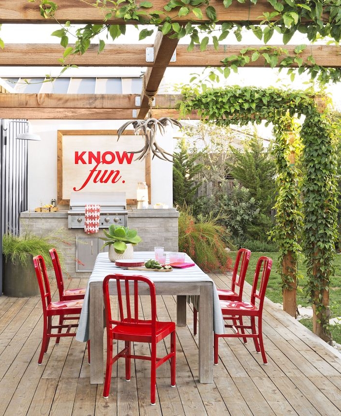 ein boden aus holz, eine miniküche mit einem tisch aus holz und mit roten stühlen, eine weiße vase mit grünen pflanzen, eine outdoor küche selber bauen