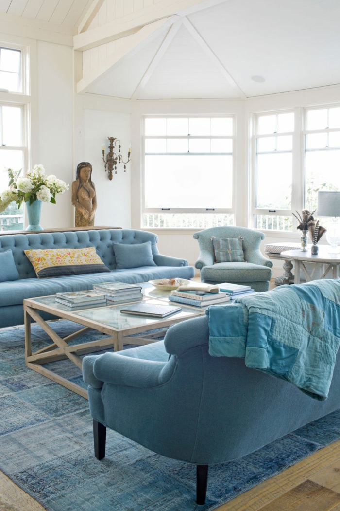 wohnzimmer modern gestalten im landhaus stil weiß und blau, großer raum mit zwei sofas, tisch dazwischen, frische blumen in vase und eine figur von frau