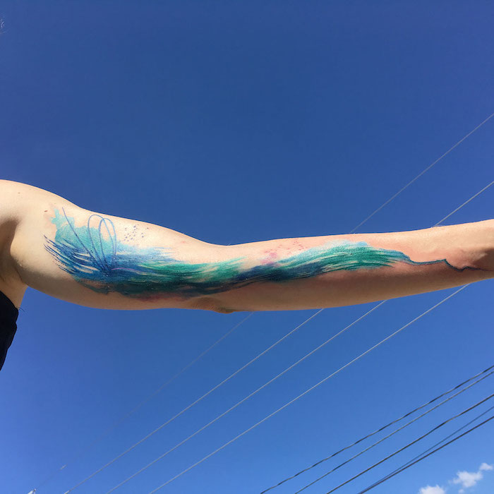 eine hand mit einem großen blauen watercolor tattoo arm mit einem blauen meer mit blauen wellen und ein blauer himmel, tattoo ideen aquarell