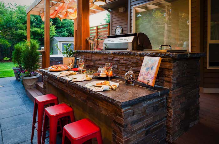 drei rote stühle und eine kleine braune miniküche ,miteinem grill, herd und einem waschbecken, ei garten mit grünen pflanzen