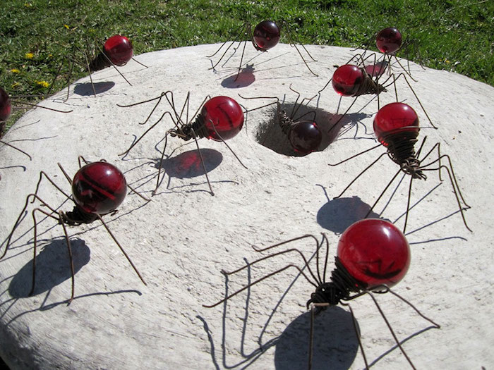 ein grauer tisch aus stein und viele große rote dekorative ameisen aus alten roten glühbirnen und mit langen schwarzen beinen, garten deko selber basteln, recycling bastreln ideen