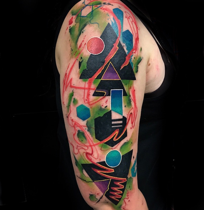 eine hand mit einem watercolor tattoo mit vielen scwarzen, roten und blauen geometrischen figuren, ein tattoo arm, ein mann mit einem schwarzen unterhemd