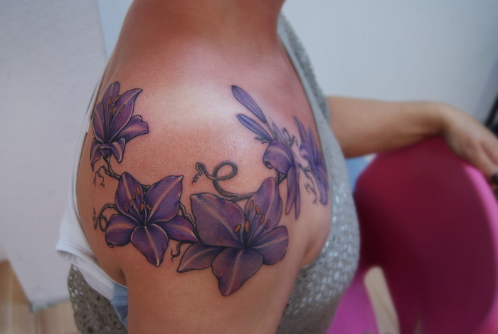 eine junge frau mit einem großen violetten watercolor tattoo arm mit vielen violetten und gelben blumen, frau und ein pinker stuhl