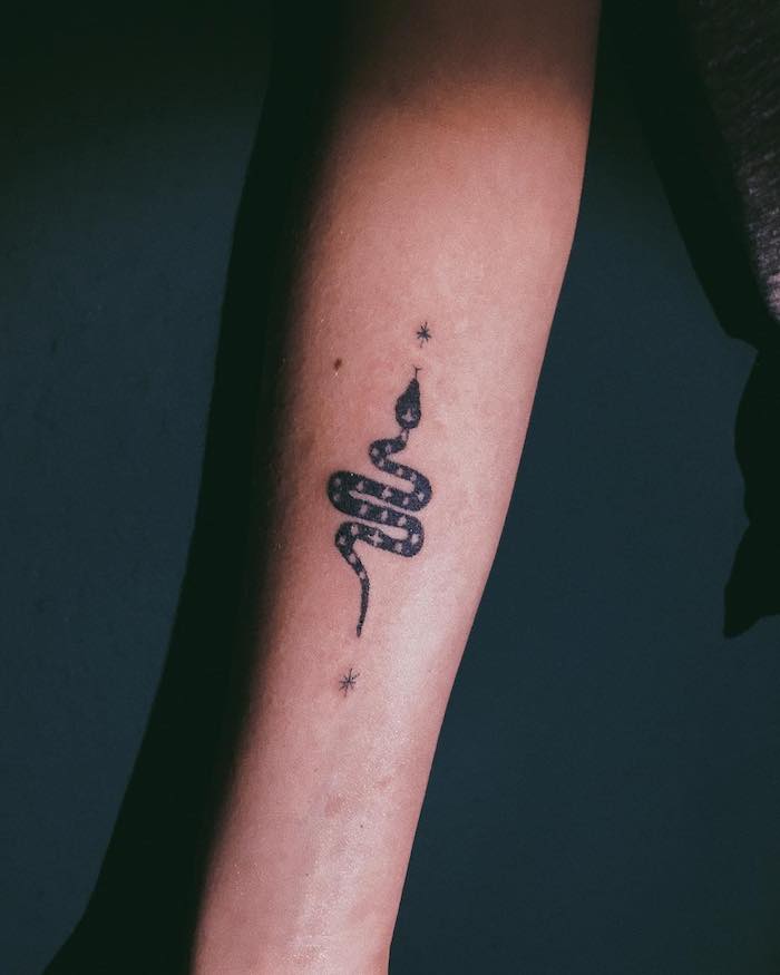 eine kleine schwarze schlange und kleine schwarze und weiße sterne, eine hand mit einem schwarzen schlange tattoo, symbol für stärke 