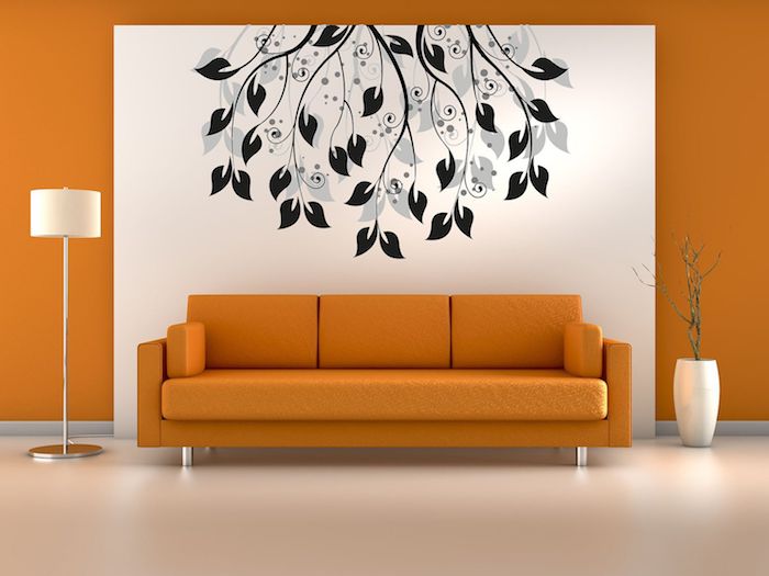 eine große orange wand und ein weißes bild mit vielen schwarzen ästen und blättern, ein oranges sofa und eine weiße lampe 