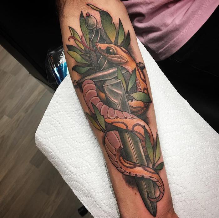 eine hand mit einem tattoo mit einem schwert und mit einer langen orangen schlange und grünen pflanzen mit grünen blättern, symbol für stärke kraft mut