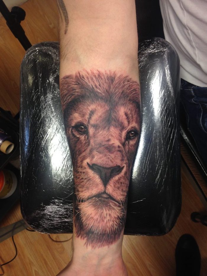 ein löwe mit schwarzen augen und mit einer schwarzen nase und einer dichten mähne, eine hand mit einem löwen tattoo, ein symbol für kraft und stärke tattoo