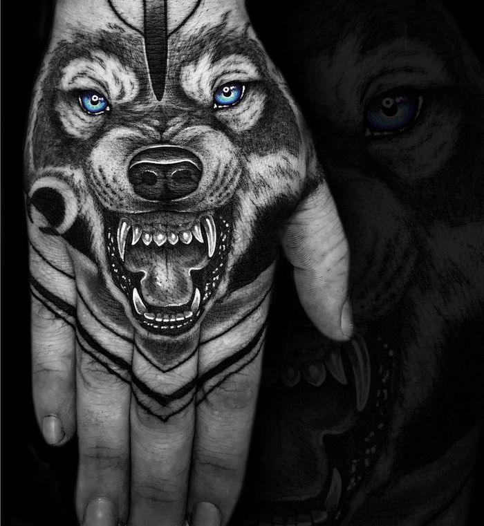 eine hand mit einem tattoo mit einem schwarzen wolf mit scharfen weißen zähnen und mit blauen augen und einer schwarzen nase 