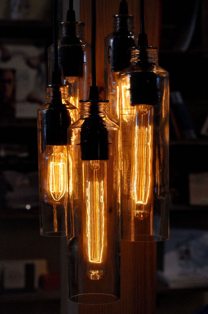 große lampe aus vielen geschnittenen alten flaschen für wein und aus glas und mit großen orangen glühbirnen