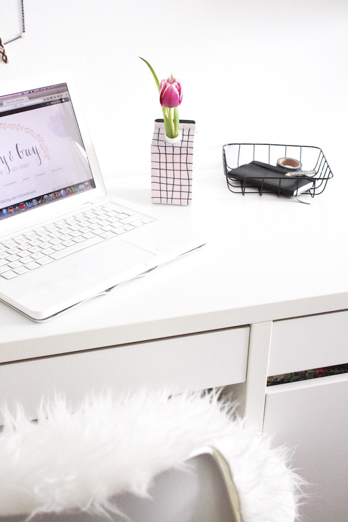 ein laptop und ein weißer schreibtisch und eine kleine weiße vase aus einem alten tetra pack und mit einer violetten tulpe mit grünen blättern