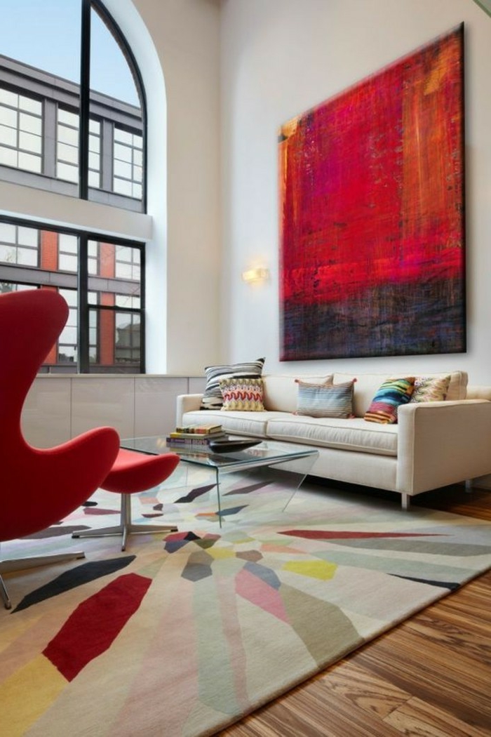 Bild in roter und schwarzer Farbe, bunter Teppich, beiges Sofa, Tisch aus Glas, roter Sessel, schöne Farbkobinationen