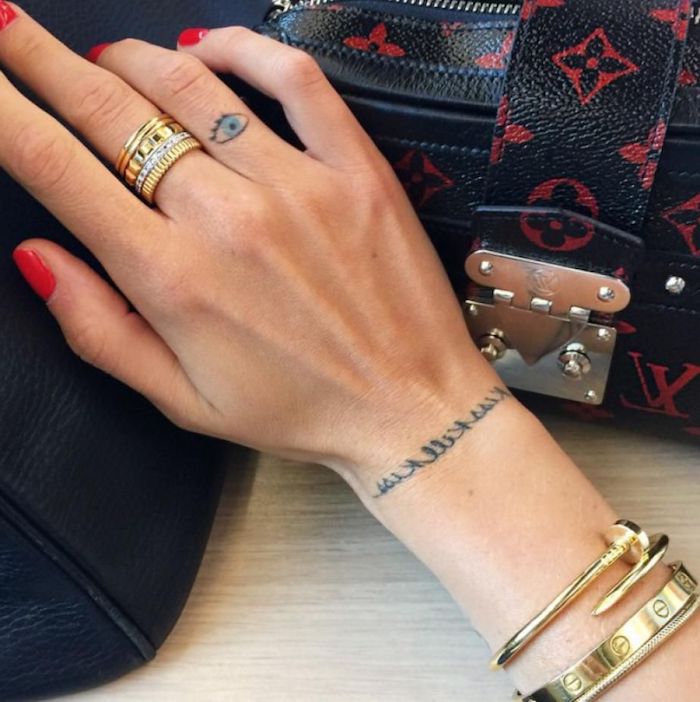 Tattoos am Ringfinger und Handgelenk, goldene Ringe und Armbänder, roter Nagellack