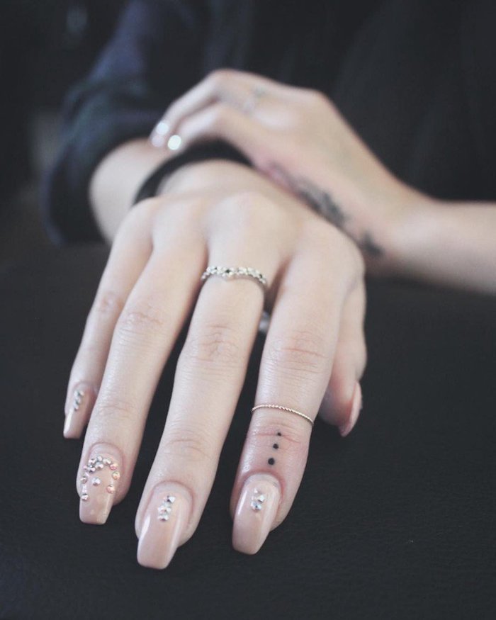 Kleines Tattoo am Zeigefinger, drei Punkte, Nagellack mit Steinen, goldene Ringe