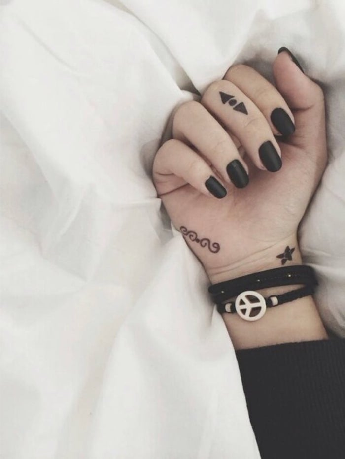 Kleine Tattoos am Mittelfinger und am Handgelenk, Armband mit Friedenszeichen, schwarzer Nagellack