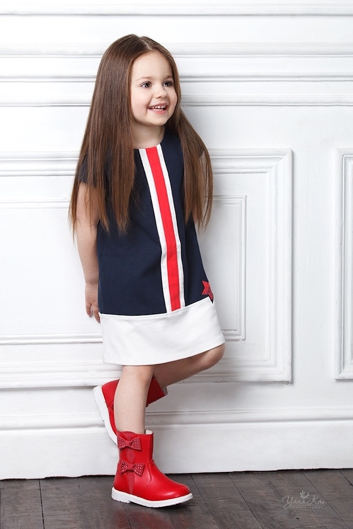 Lange glatte Haare mit Mittelscheitel, dunkelblaues Kleid mit roten und weißen Kanten, rote Stiefel mit Schleifen