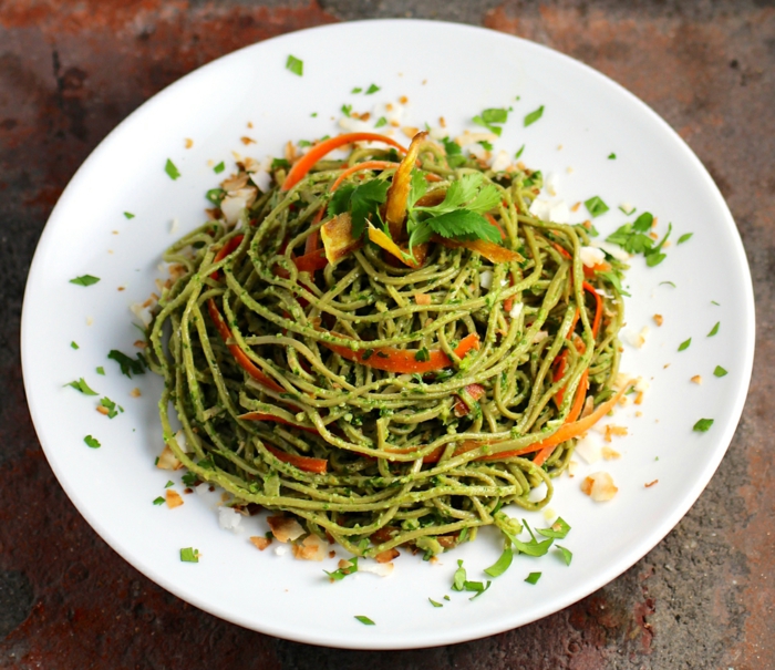 ein vegan Gericht, grüne Nudeln mit Pestosoße, Karoten auf Scheiben, Fitness Gerichte