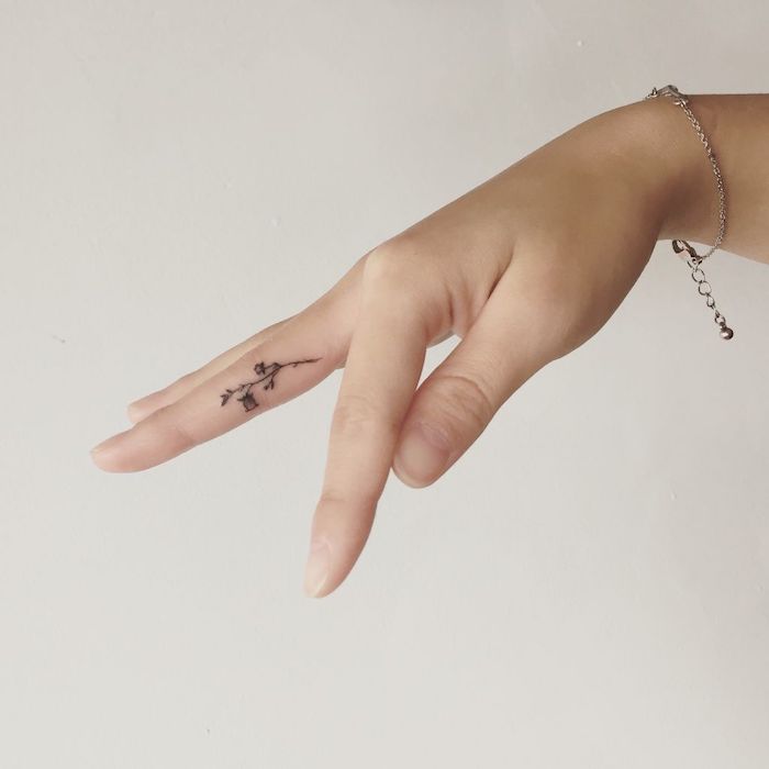 Kleines Blumen Tattoo am Mittelfinger, Tattoo Motive für Frauen, silbernes Armband