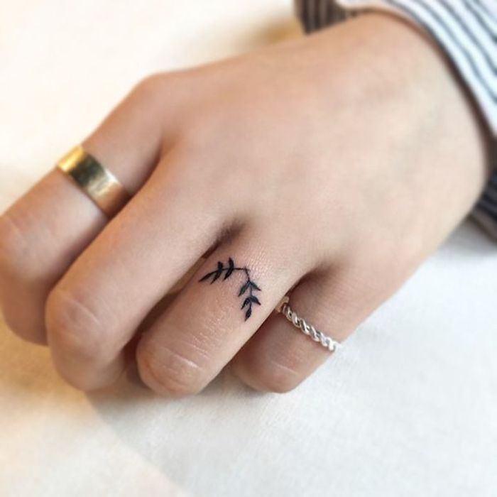 Kleines schwarzes Tattoo am Ringfinger, goldener und silberner Ring