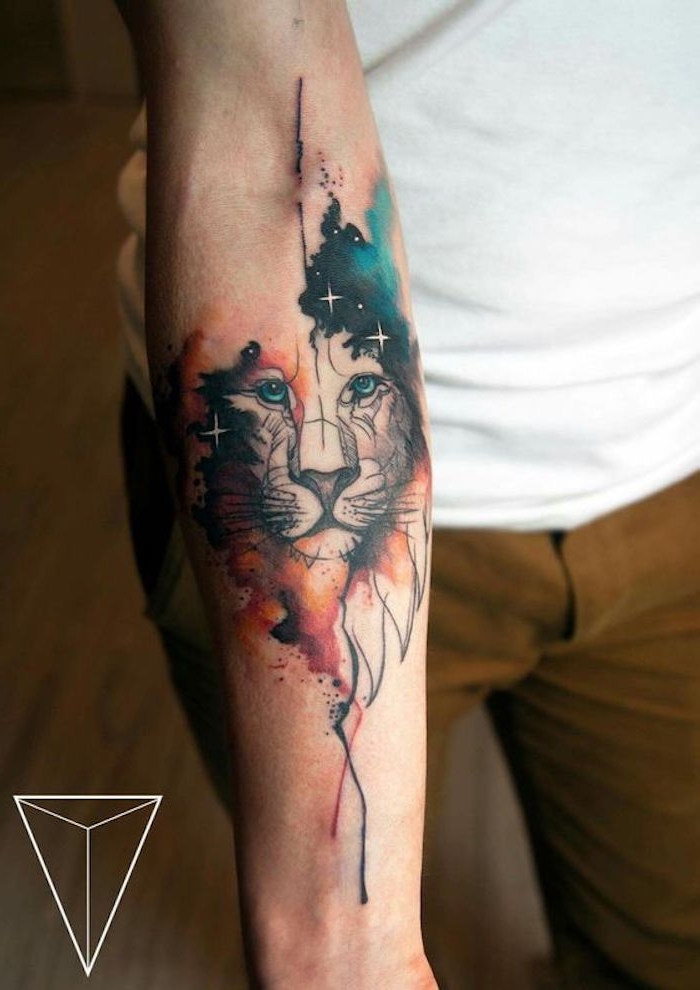 eine hand mit einem großen watercolor tattoo mit löwe mit blauen augen und einer roten mähne und mit einem himmel mit vielen kleinen weißen sternen 