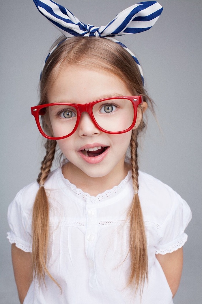 Tolle Kinderfrisuren zum Nachstylen, zwei Zöpfe und gestreiftes Haarband, weißes Hemd mit kurzen Ärmeln, Brille mit rotem Rahmen