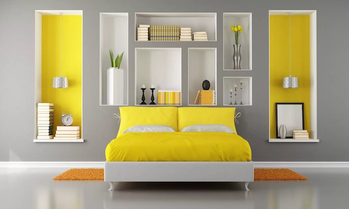 eine große graue wand in einem schlafzimmer mit einem gelben bett mit gelben und weißen kissen, weiße vase mit grünen pflanzen und gelben blumen, wandfarbe gelb