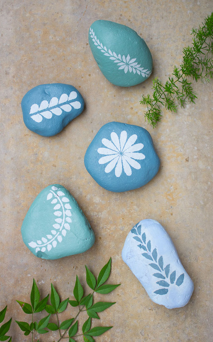 Steine bemalen, blaue Steine mit weißen Blumenmotiven, schöne Deko für den Garten