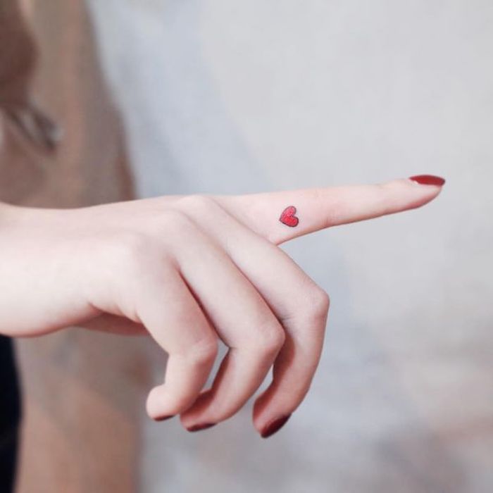 Kleines farbiges Tattoo am Zeigefinger, rotes Herz, roter Nagellack, Tattoo Ideen für Frauen