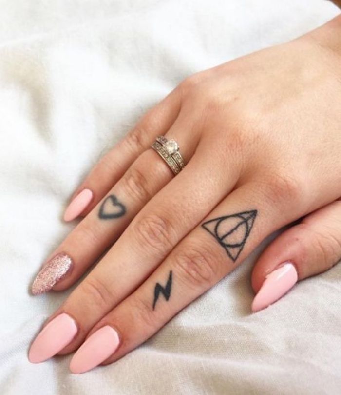 Kleine Tattoos am Zeigefinger und Ringfinger, rosafarbener Nagellack, ein Nagel mit Glitter