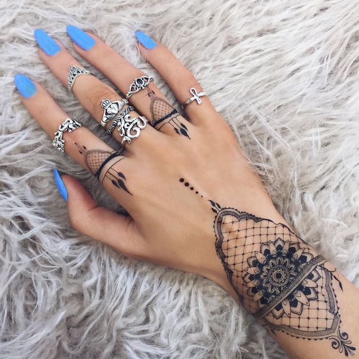 Mandala Tattoo an der Hand, viele silberne Ringe, blauer Nagellack, spitze Nägel