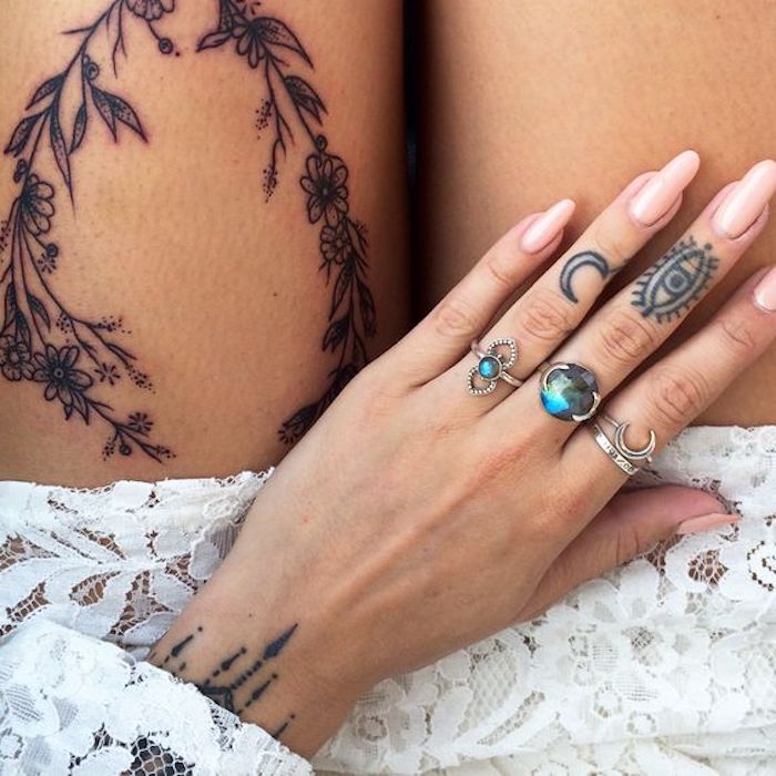 Tattoos an Fingern und Oberschenkel, drei silberne Ringe, rosafarbener Nagellack, weißes Spitzenkleid