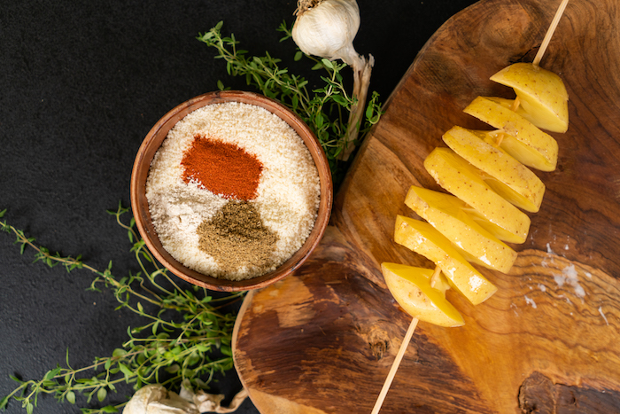 Geräucherter Paprika, Knoblauchpulver und gemahlener Kreuzkümmel in den Parmesan einrühren, die Kartoffel mit geschmolzener Butter bepinseln 