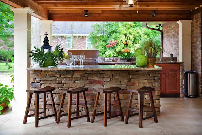 vier braune stühle aus holz und ein tisch aus steinen, gläser und grüne pflanzen, eine außenküche holz