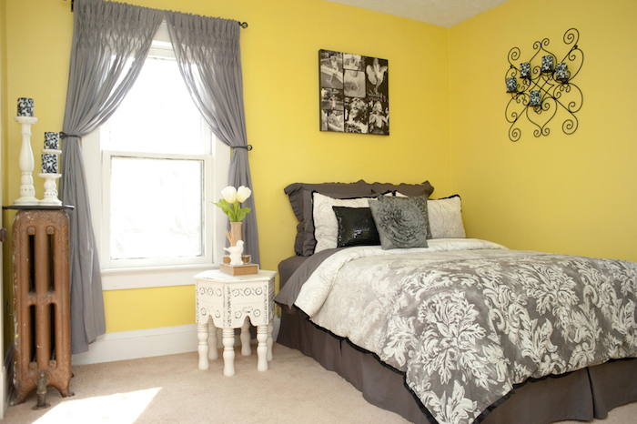 schlafzimmer mit gelben wänden und mit einem bett mit einer grauen decke mit weißen blumen und schwarzen und weißen kissen, wandfarbe schlafzimmer