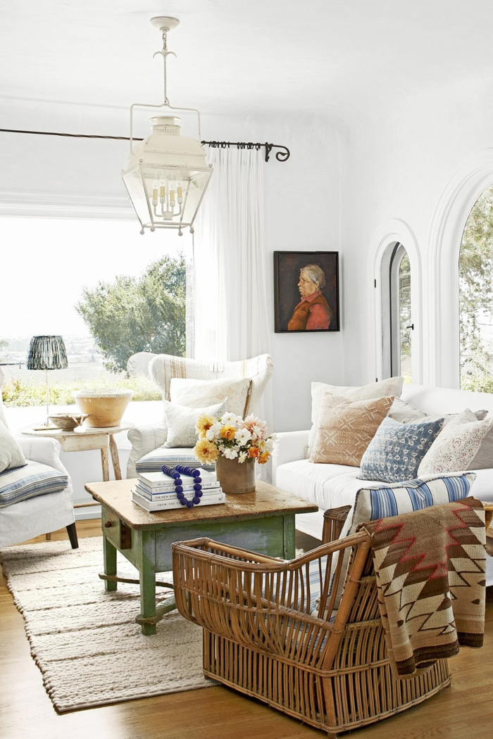 ein helles und breites wohnzimmer modern gestaltet, weiße farbe überwiegend, weiße wände, vintage tisch mit schublae, bild an der wand selbst gemalt, rattan sessel